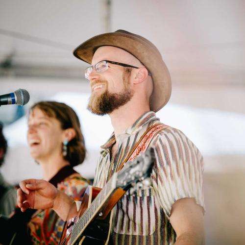man with guitar smiling on stage with band member in background