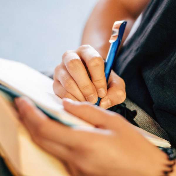 hands with blue pen writing in notebook