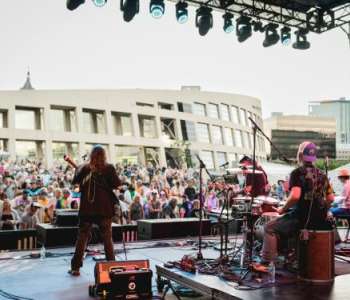 Blonde woman playing guitar with band members in the background